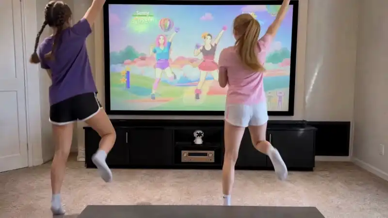 Two kids playing a motion-controlled dance game in front of the TV — the Plaik camera AI tracks their full-body movement in real time